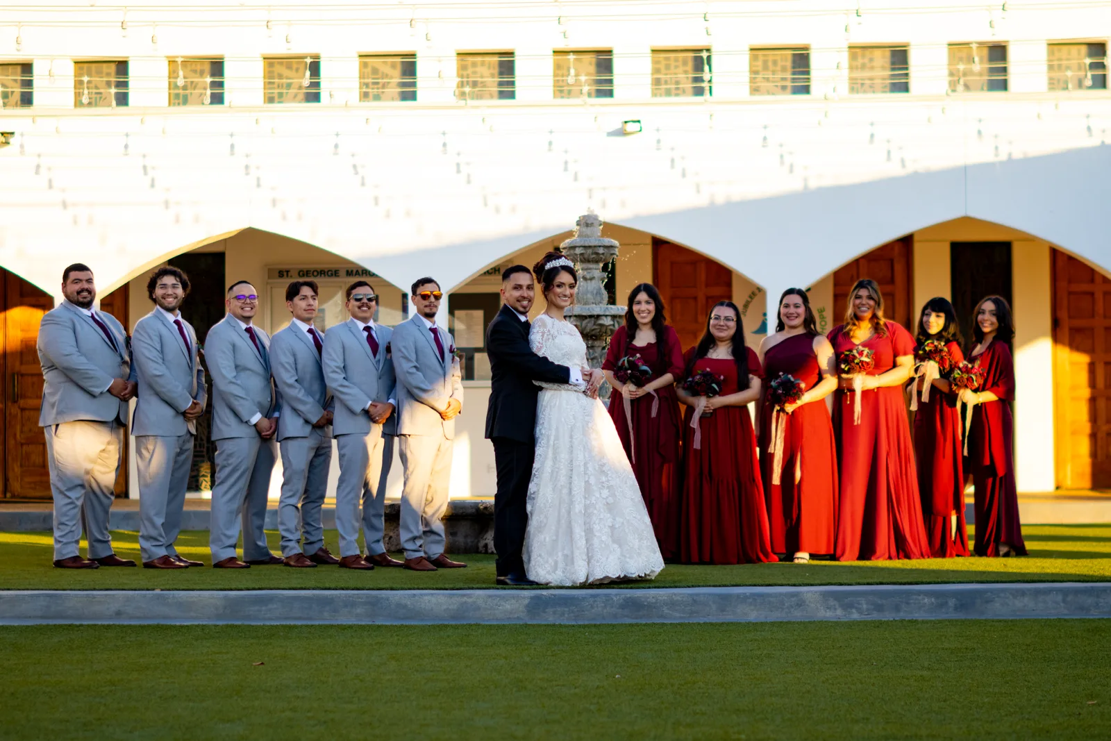 A newly married couple with their full wedding party at a church courtyard fountain